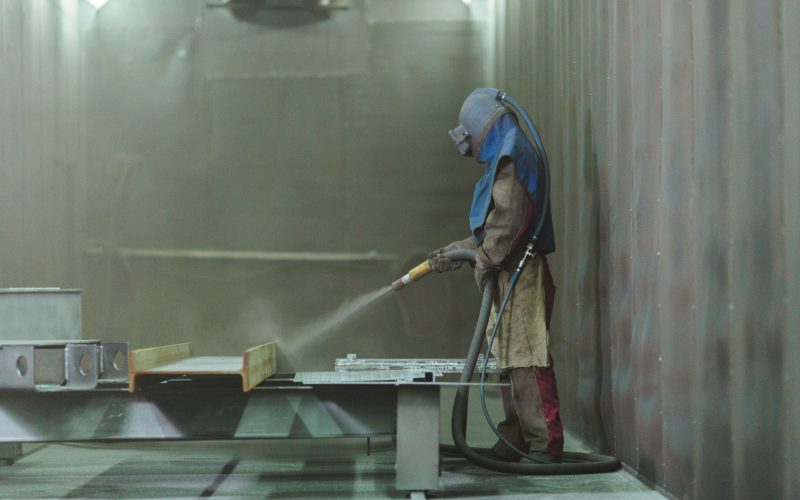 Sandblast. Blasting metal. An employee prepares a metal part for painting. A harsh man works in the factory.